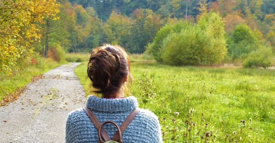 Vrouw met rugzak kijkt uit over een rustig pad en herfstlandschap – symbool voor de weg van verlies, stil verdriet en verborgen rouw.