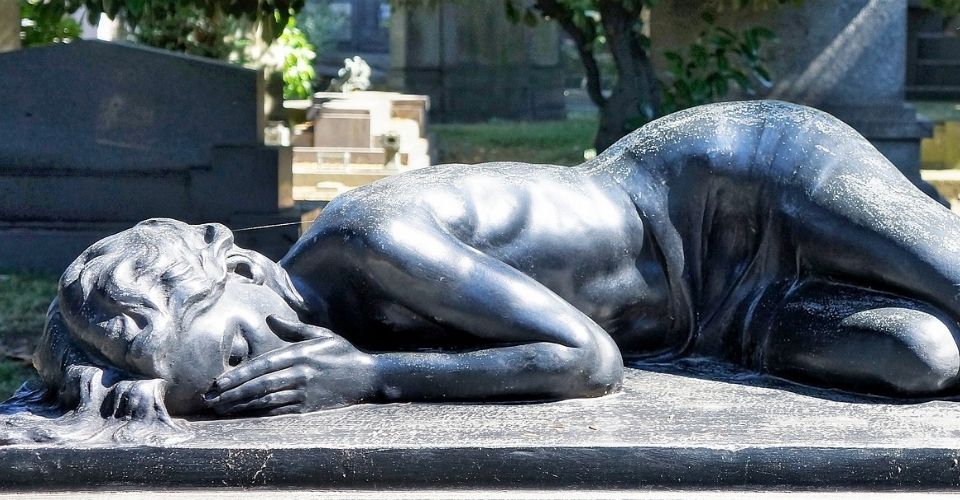 Zwarte grafsculptuur van een vrouw die haar gezicht bedekt – een krachtige metafoor voor het intense gevoel van alleen zijn in rouw.