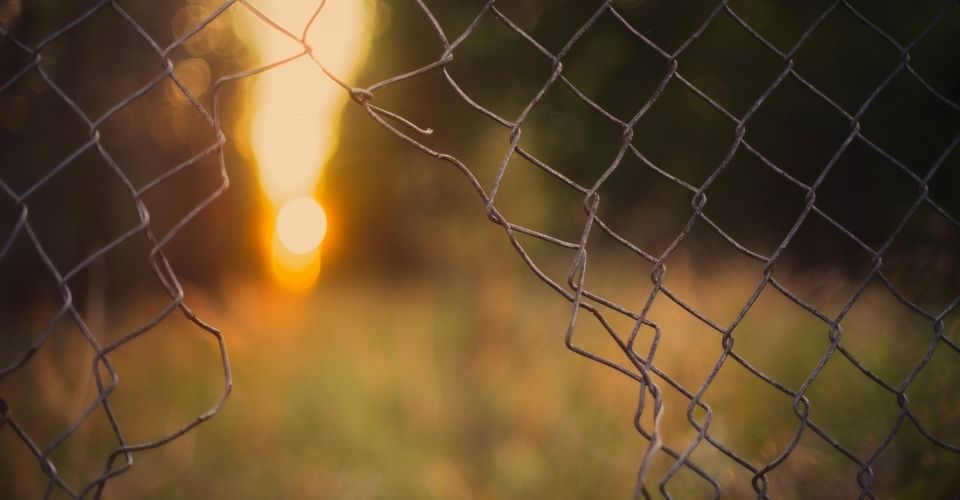 Een gebroken hekwerk met openingen waar het zonlicht doorheen valt – symbolisch voor hoe we soms over onze eigen grenzen heen laten gaan.