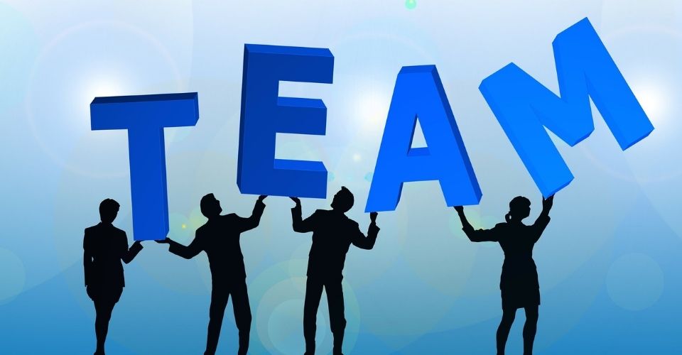 Vier mensen tillen samen de letters van TEAM – beeld van teamdynamiek bij organisatieverandering