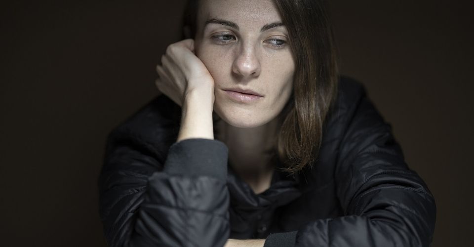 Vrouw kijkt peinzend en afwezig voor zich uit – gevangen tussen onvrede en het (onbewuste) gemak van alles bij het oude laten.