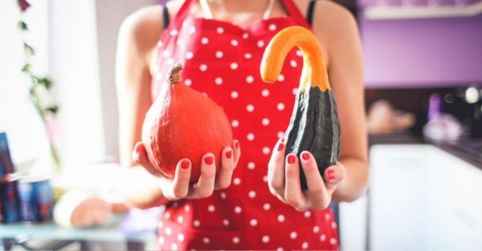 Vrouw in keukenschort houdt twee verschillende pompoenen vast – speels beeld dat laat zien dat normaal zijn een kwestie van perspectief is.