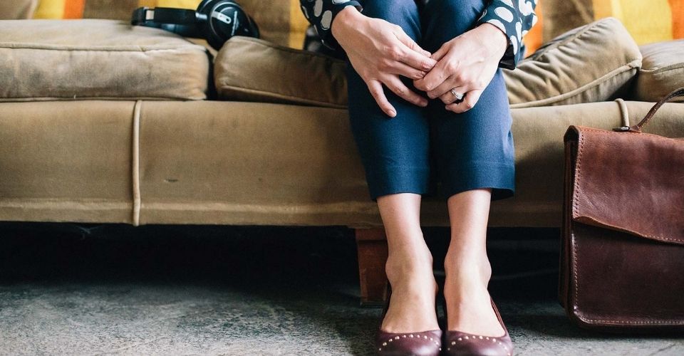 Vrouw zit met ineengevouwen handen op een bank – beeld van twijfel en de innerlijke stem die zegt: het gaat me toch niet lukken.