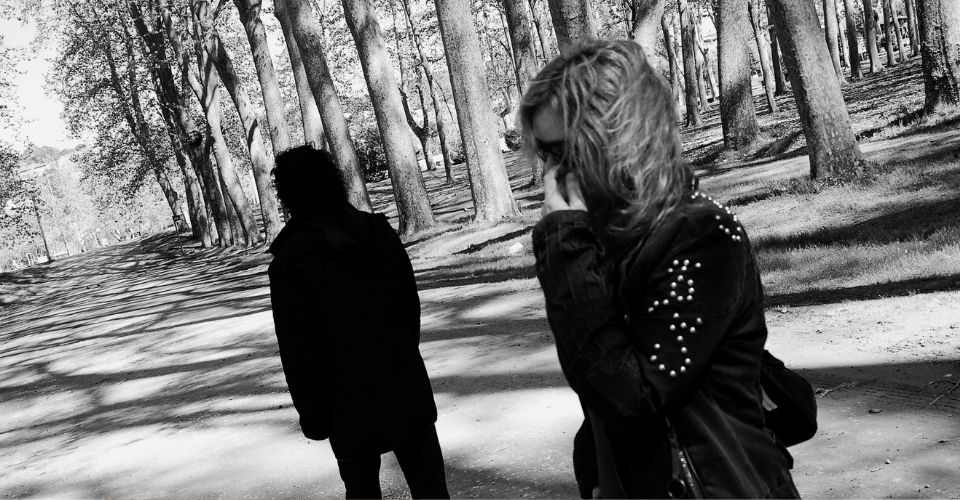 Vrouw kijkt verdrietig weg van man terwijl ze in een park loopt – boosheid die eigenlijk op zichzelf gericht is.