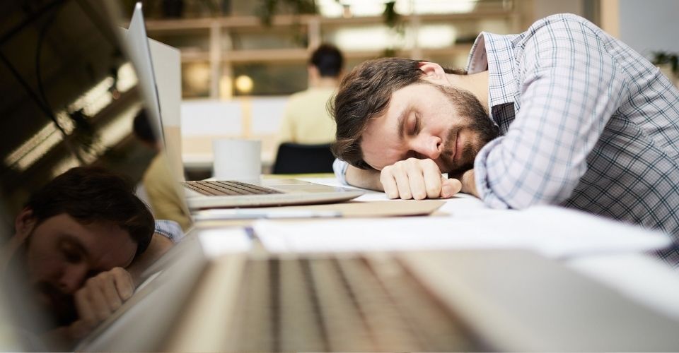 Man ligt uitgeput met hoofd op bureau tussen laptops – relatieproblemen kunnen leiden tot stress en uitputting op het werk.