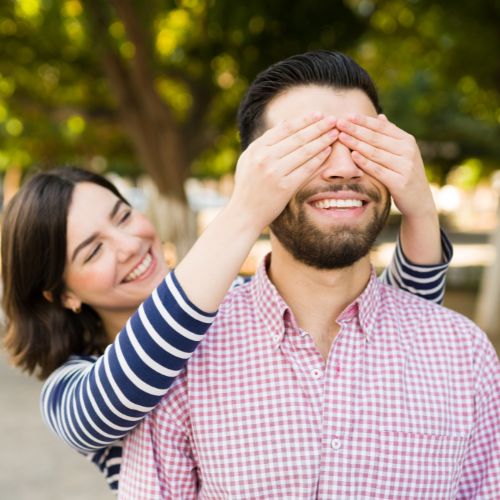 Beeld van een vrouw die haar handen voor de ogen van haar partner houd om hem ergens mee te verrassen. Een belangrijk element van een sterke relatie.