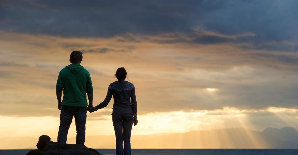 Koppel hand in hand op een rots bij zee – beeld van een relatie waarin samen stappen buiten de comfortzone zorgen voor groei en verbinding.
