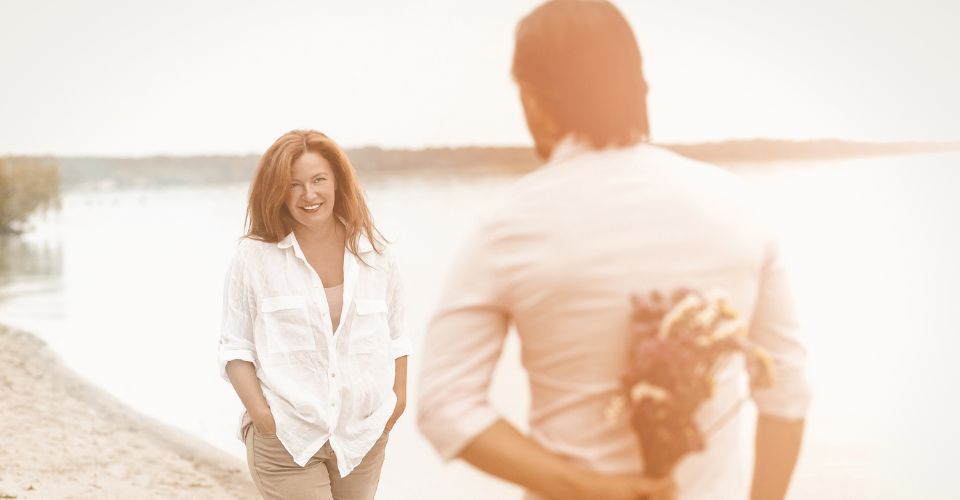 Man houdt een bos bloemen achter zijn rug terwijl hij zijn partner benadert – verrassing als krachtig gebaar binnen een liefdevolle relatie.