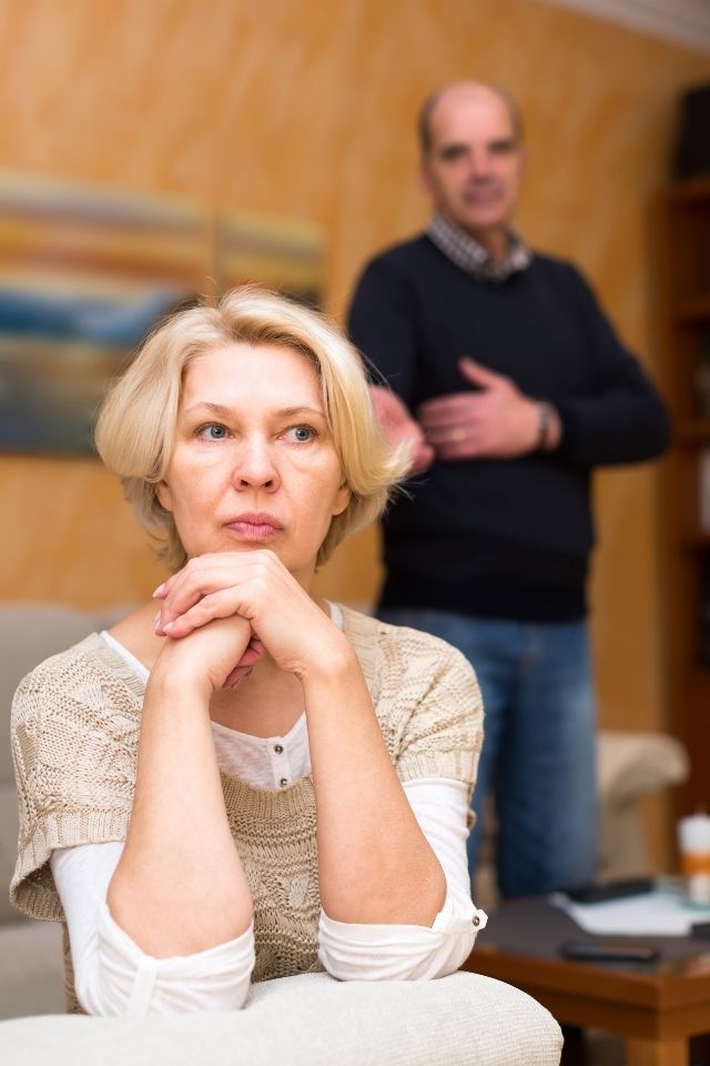 gebrek aan bereidheid relatie uitgedoofd Afwezige blik bij vrouw terwijl partner op de achtergrond staat – voorbeeld van een relatie waarin geen bereidheid is om verder te investeren.