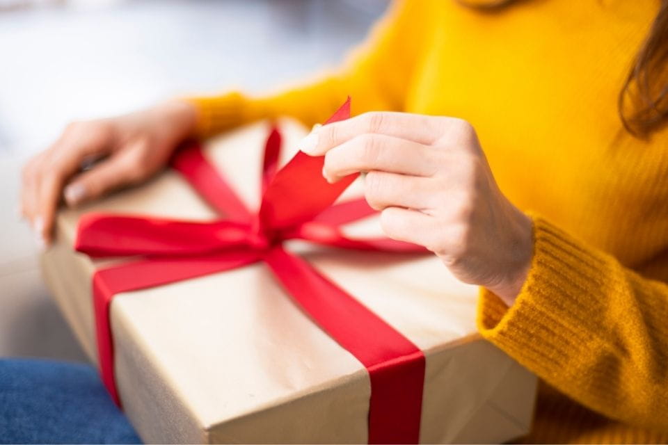 Handen openen een cadeau-doos met rode strik: ontvang de Toolkit Grip op Communicatie voor betere relatiecommunicatie